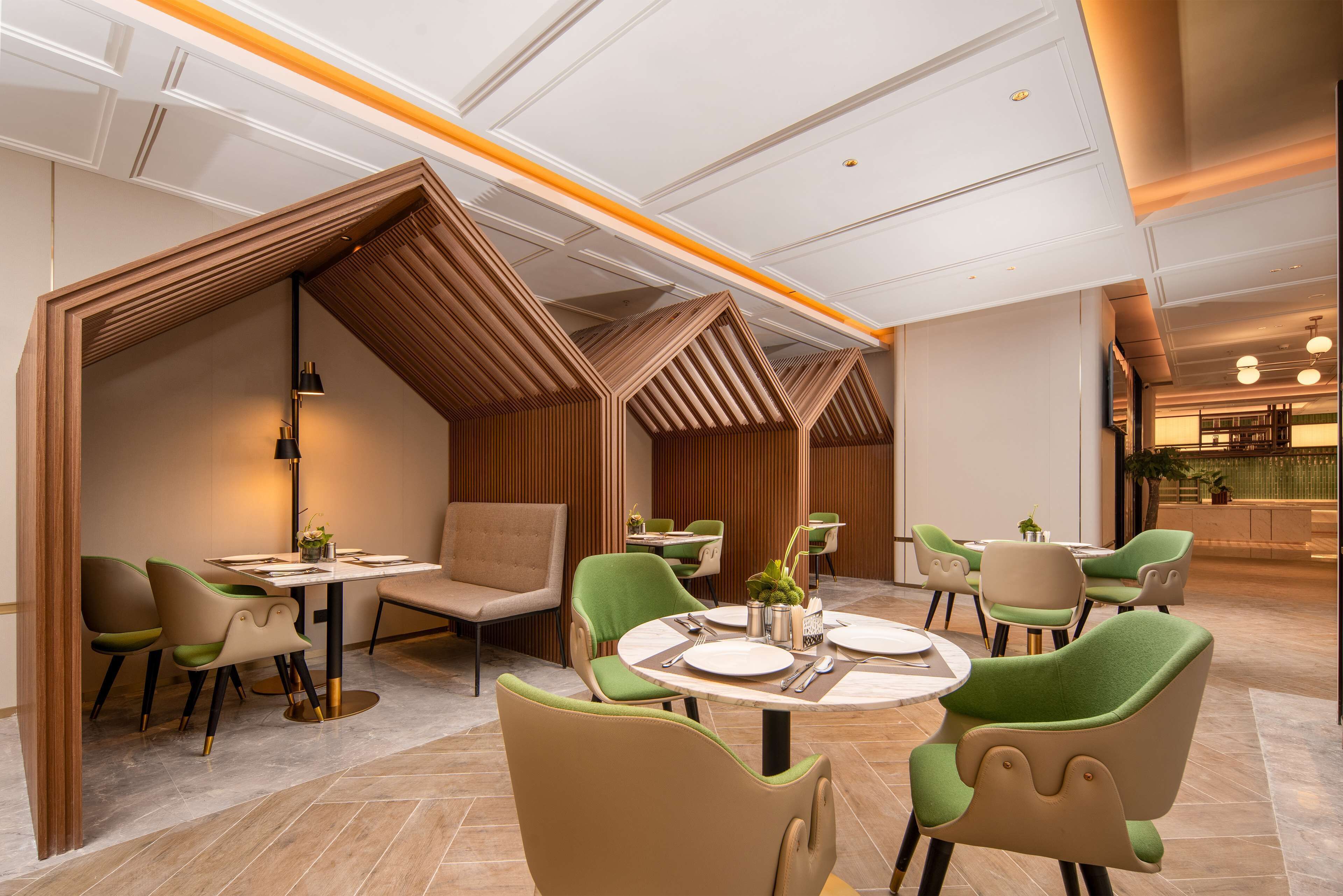 A modern restaurant with booths and round tables, featuring a geometric ceiling design and a warm color palette.