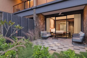 A modern outdoor patio with a sofa and chairs, a stone wall, and a view into the interior.
