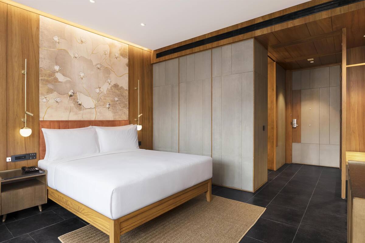 Une chambre à coucher moderne avec un cadre de lit en bois, une table de chevet, une lampe fixée au mur et une grande armoire.