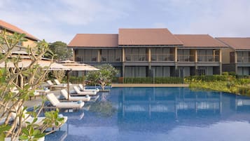 A hotel with a swimming pool, lounge chairs, and a building with a tiled roof.