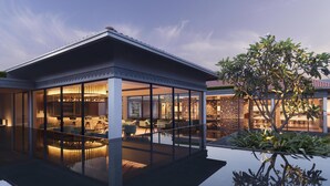 Ein modernes Haus mit Poolbereich, der von Glasflächen umschlossen ist, einem hellen Innenraum und einem großen Baum im Vordergrund.