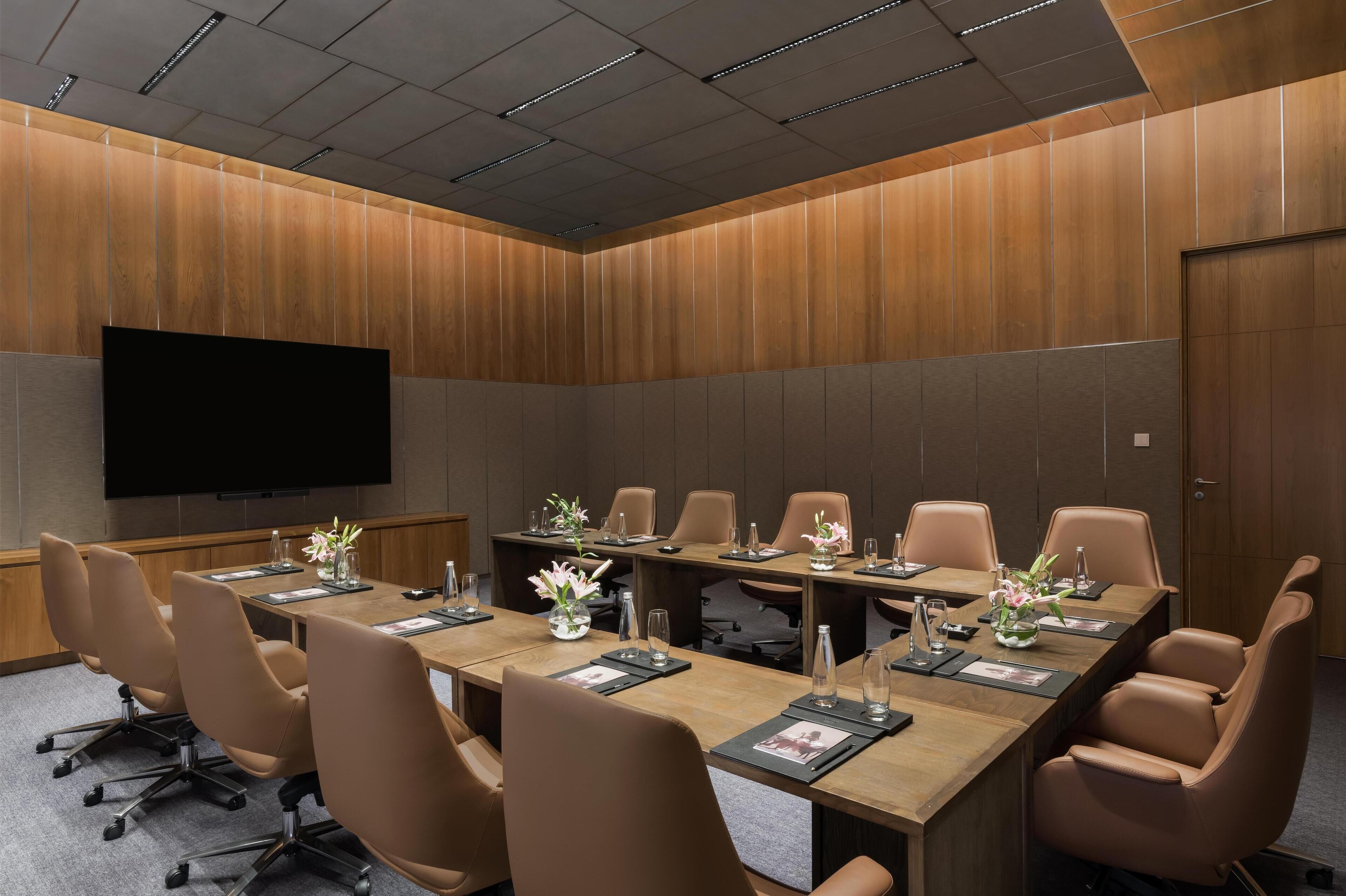 A conference room with a long table, leather chairs, and a flat-screen TV on the wall.
