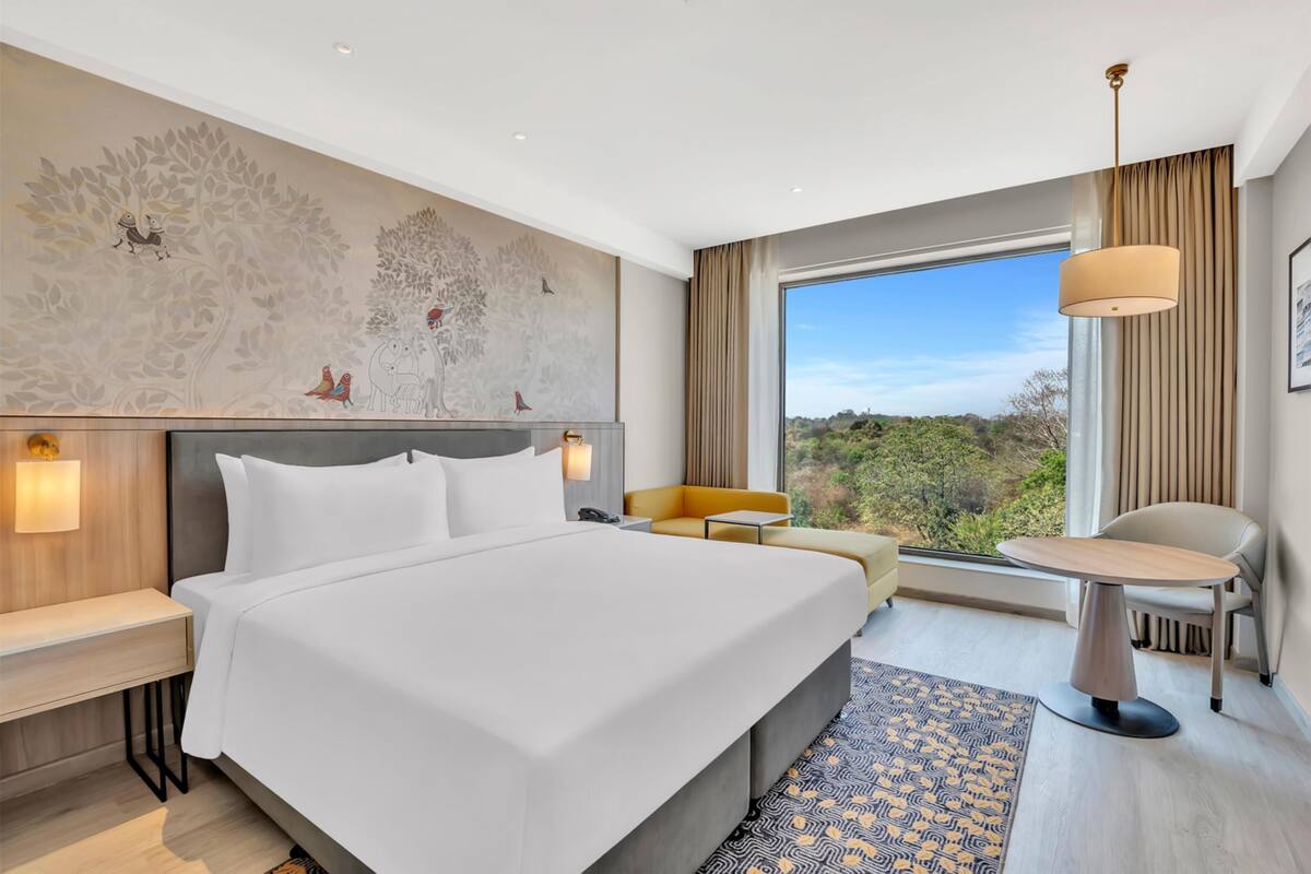 A modern hotel room with a large bed, a desk, a sofa, and a dining table.