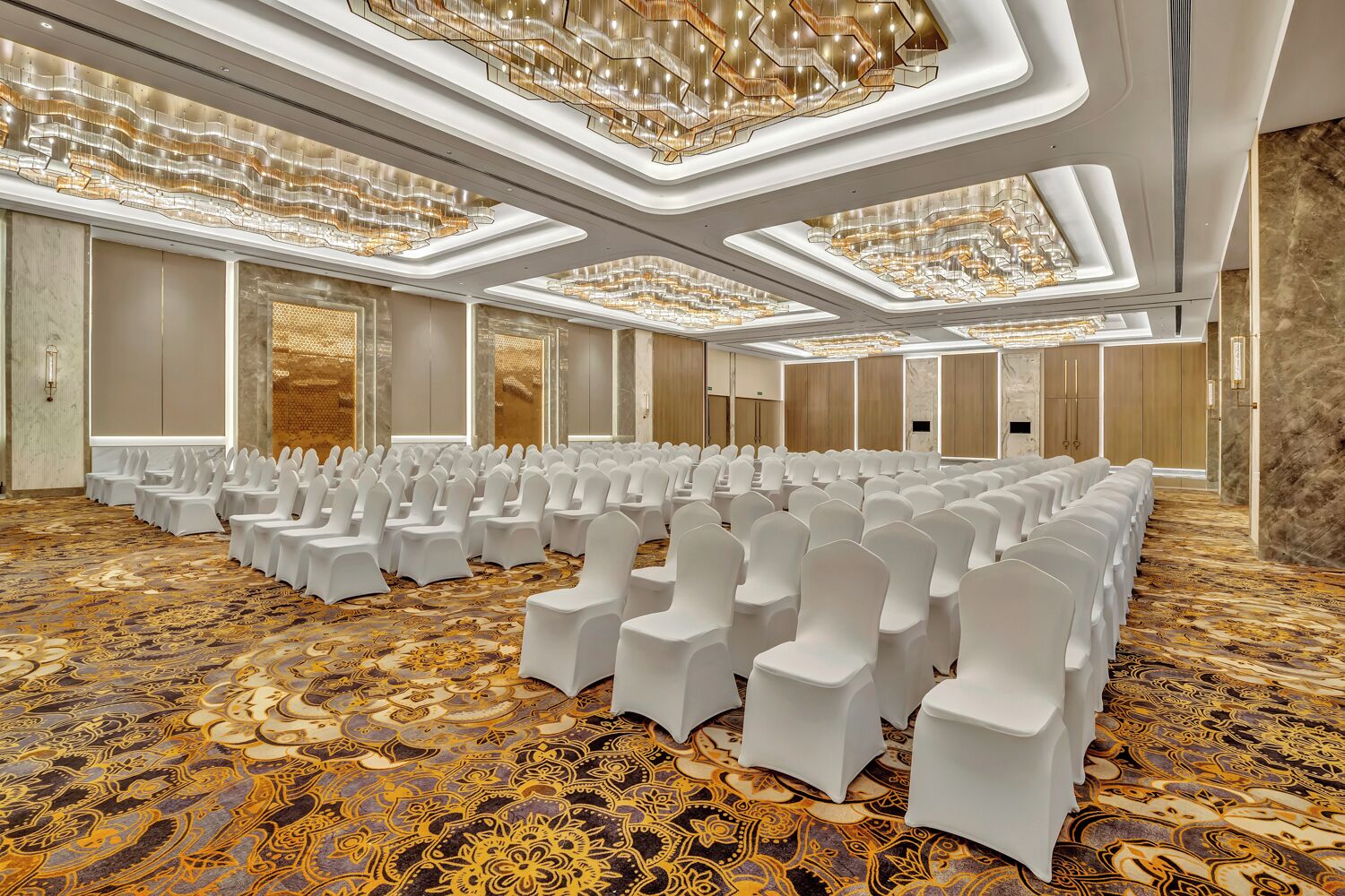 A large conference room with rows of white chairs, a patterned carpet, and a modern chandelier.
