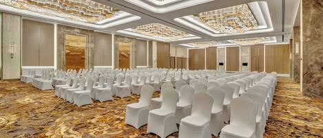 A large conference room with rows of white chairs, a patterned carpet, and a modern chandelier.