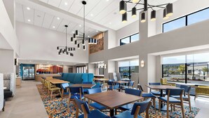 A spacious indoor area with multiple seating arrangements, including tables and chairs, and a central seating area with a sofa. - Hampton Inn & Suites Corona, Ca (Corona)