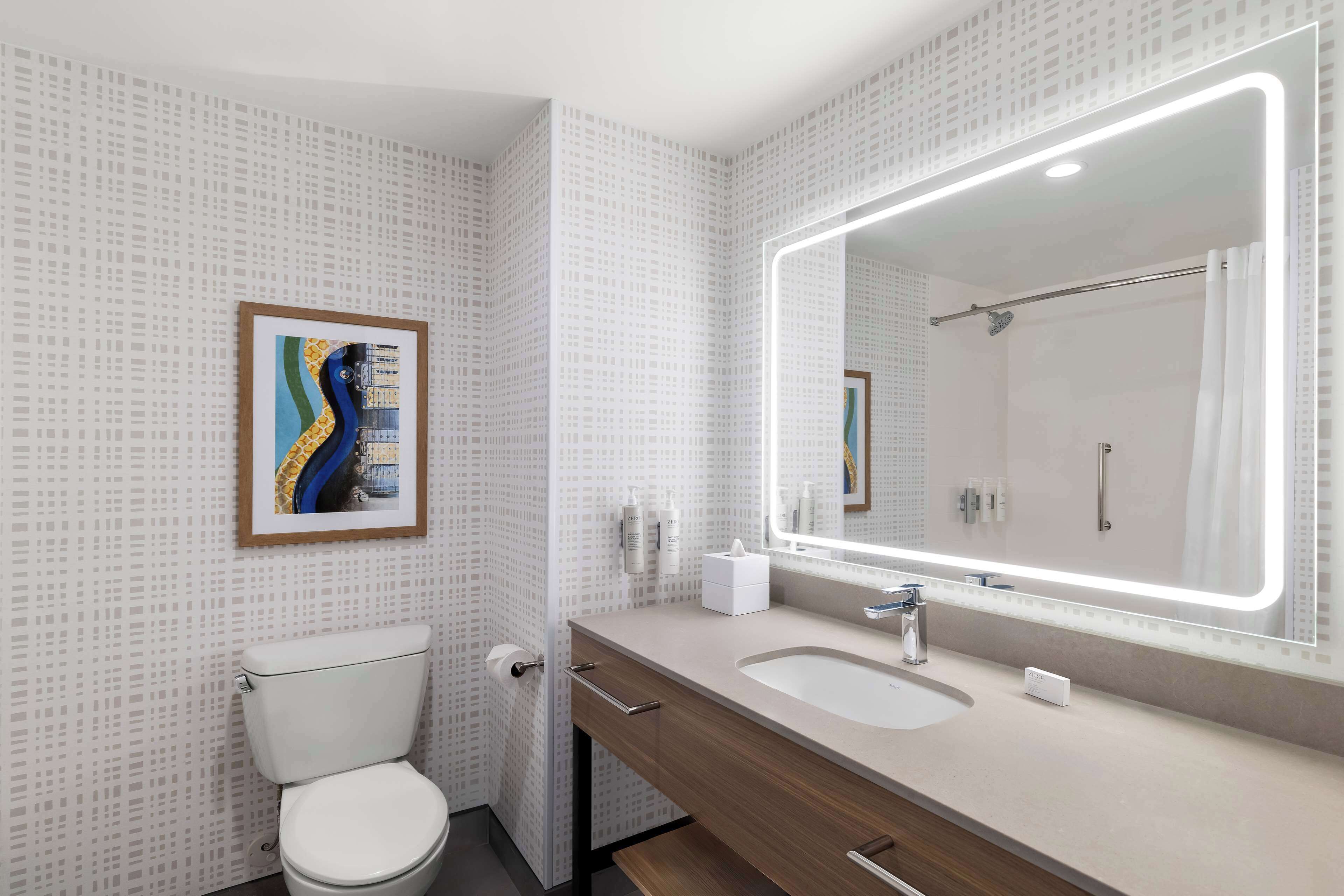 Ein modernes Badezimmer mit Toilette, Waschbecken und Spiegel sowie einem gerahmten Kunstwerk an der Wand.