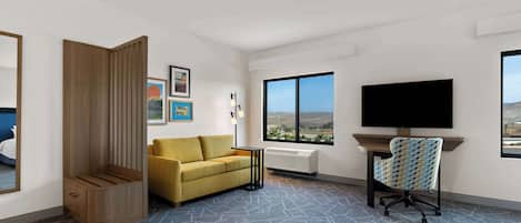 A modern hotel room with a large window, a sofa, a TV, and a desk.