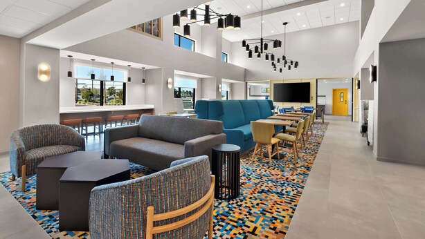 A modern hotel lobby with seating areas, a bar, and a large TV screen. - Hampton Inn & Suites Corona, Ca (Corona)