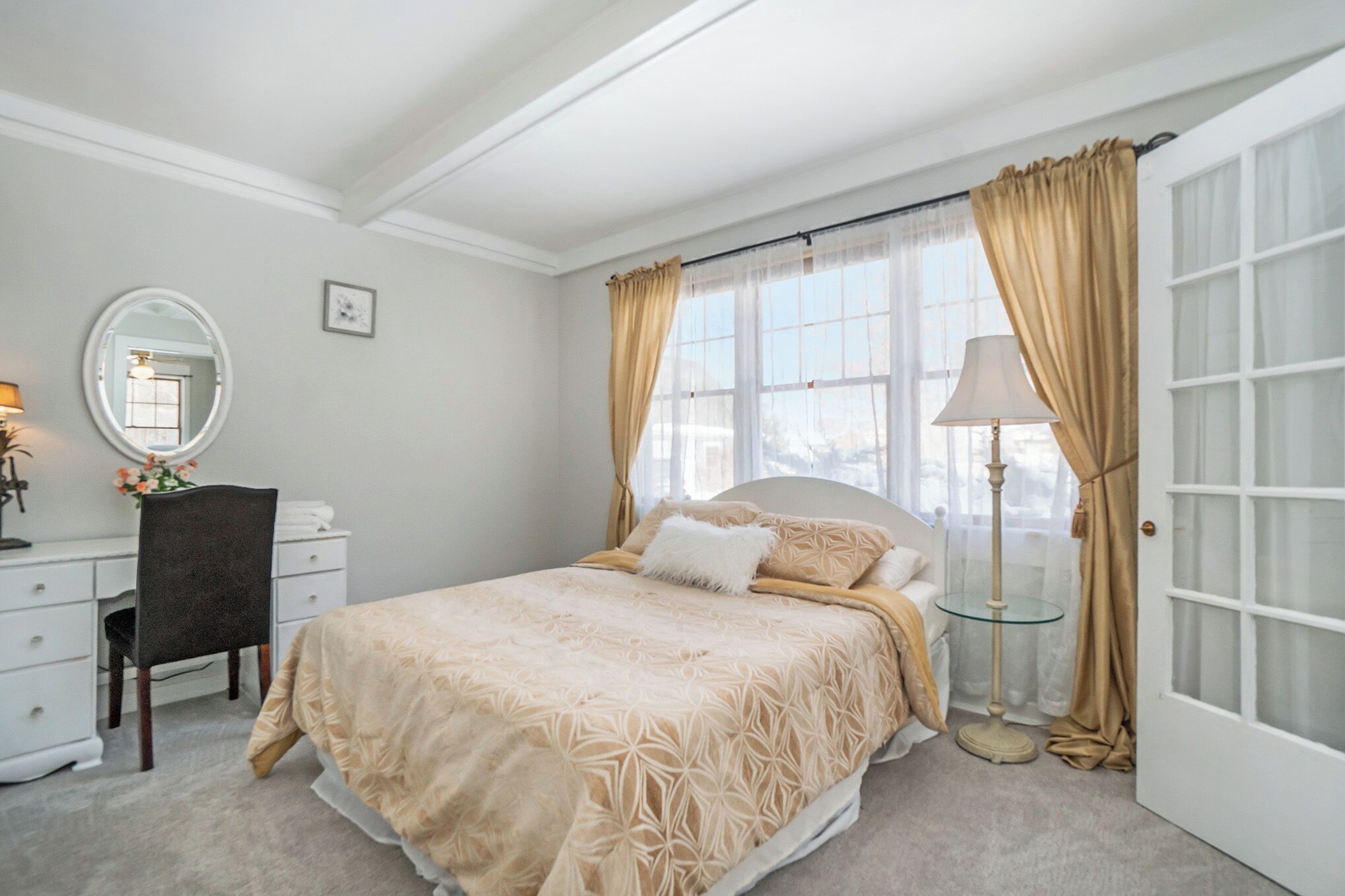 A bedroom with a bed, a desk, a chair, a lamp, and a mirror.