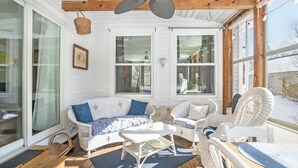 A covered porch with wicker furniture, a ceiling fan, and large windows.