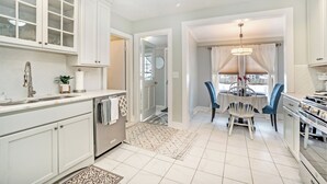 A kitchen with white cabinets, a dining area with a chandelier, and a view through a window.