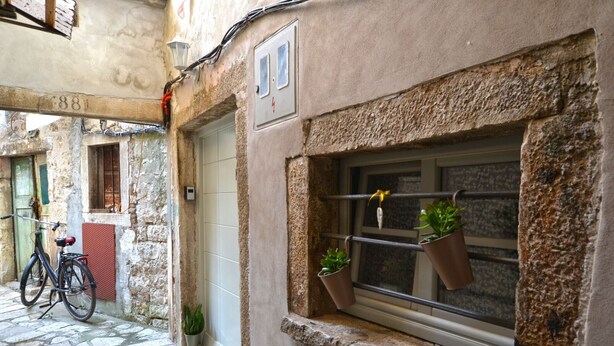 Une rue étroite avec un bâtiment en pierre, un vélo et un pot de fleurs placé près de la fenêtre.