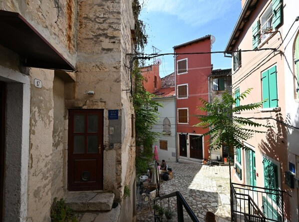 A narrow street with stone buildings, a visible door, and a small outdoor seating area with tables and chairs. - Radiant and Trendy Downtown Rovinj Apartment - One Bedroom Apartment (Rovinj)