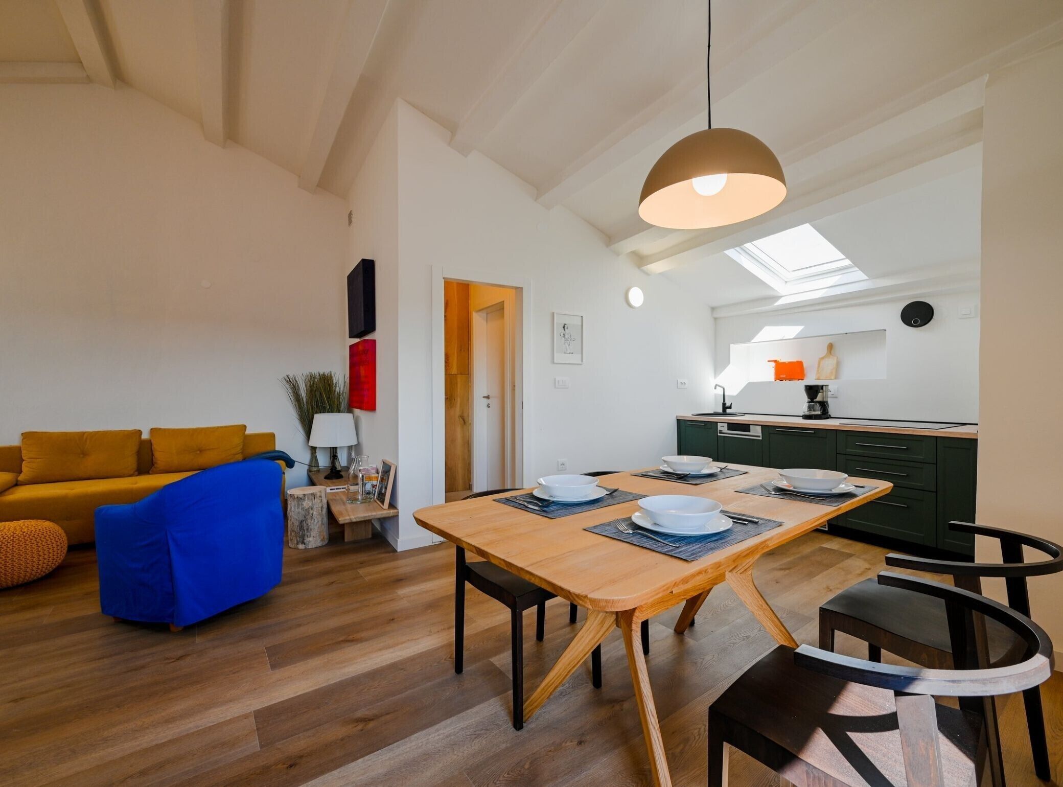 Una sala de estar moderna con una mesa de comedor de madera, un sofá azul y una cocina al fondo.
