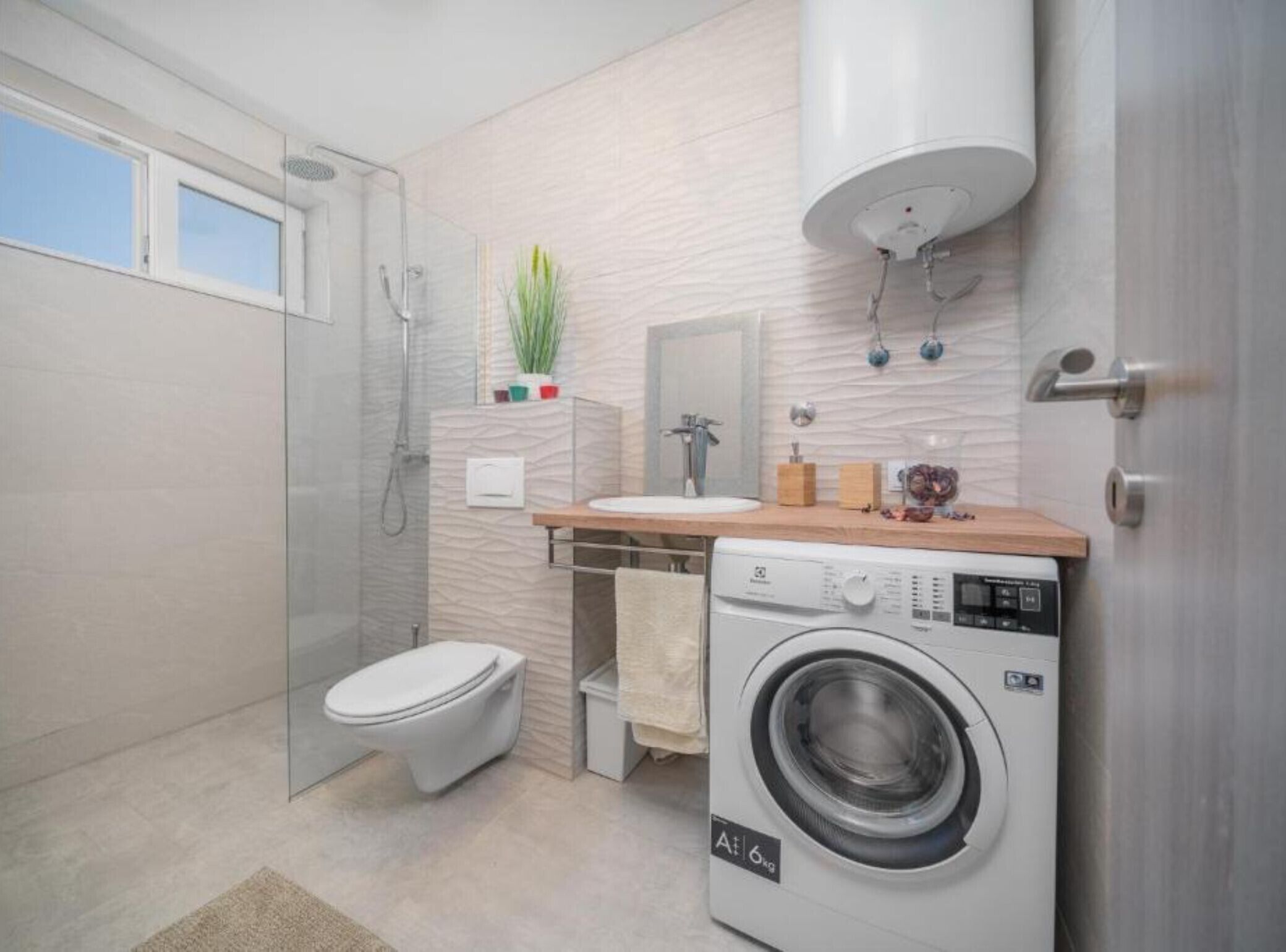 Un baño moderno con cabina de ducha de vidrio, inodoro, lavadora y lavamanos con encimera de madera.