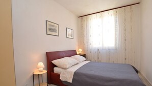Ein Schlafzimmer mit einem Bett, zwei Nachttischlampen, einem kleinen Tisch und einem Fenster mit Vorhängen.
