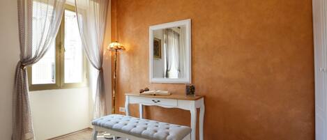 A room with a wooden bench, a bedside table, a lamp, and a mirror on the wall.