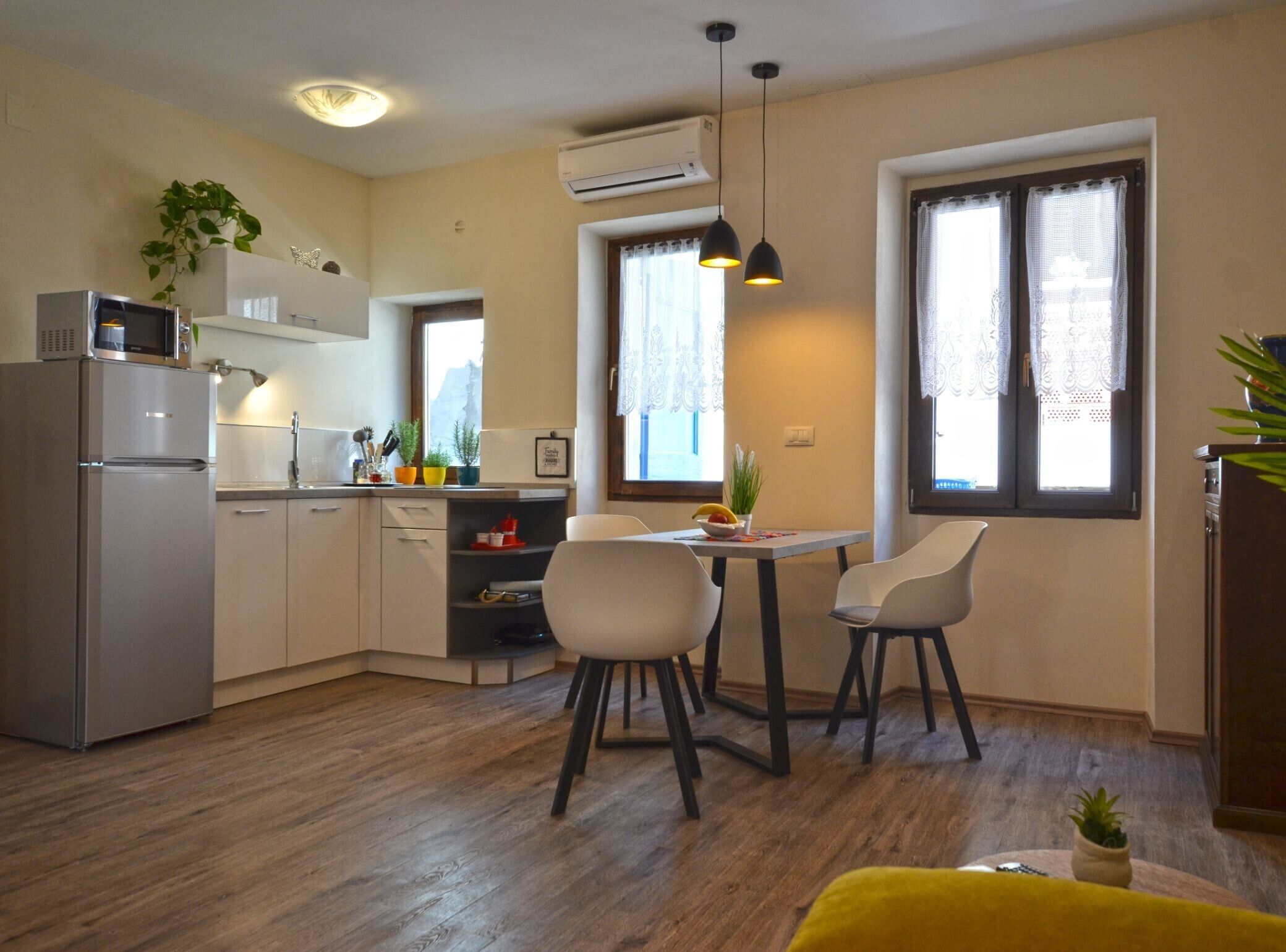 Eine kompakte Küche mit modernen Geräten, ein Essbereich mit zwei Stühlen und ein Fenster mit Spitzenvorhängen.
