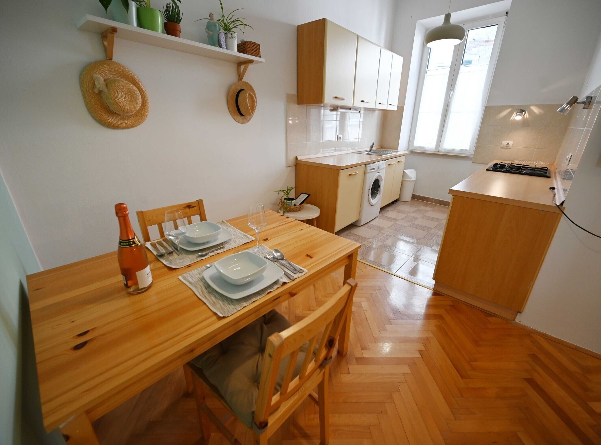 A compact kitchen with wooden cabinets, a washing machine, and a dining area with a wooden table set for two.