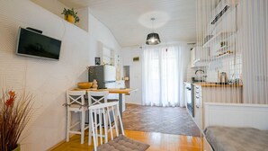 A modern living room with a dining area, a TV mounted on the wall, and a kitchen area with a stove and cabinets. - Snug and Stylish Downtown Rovinj Apartment - One Bedroom Apartment with Balcony (Rovinj)