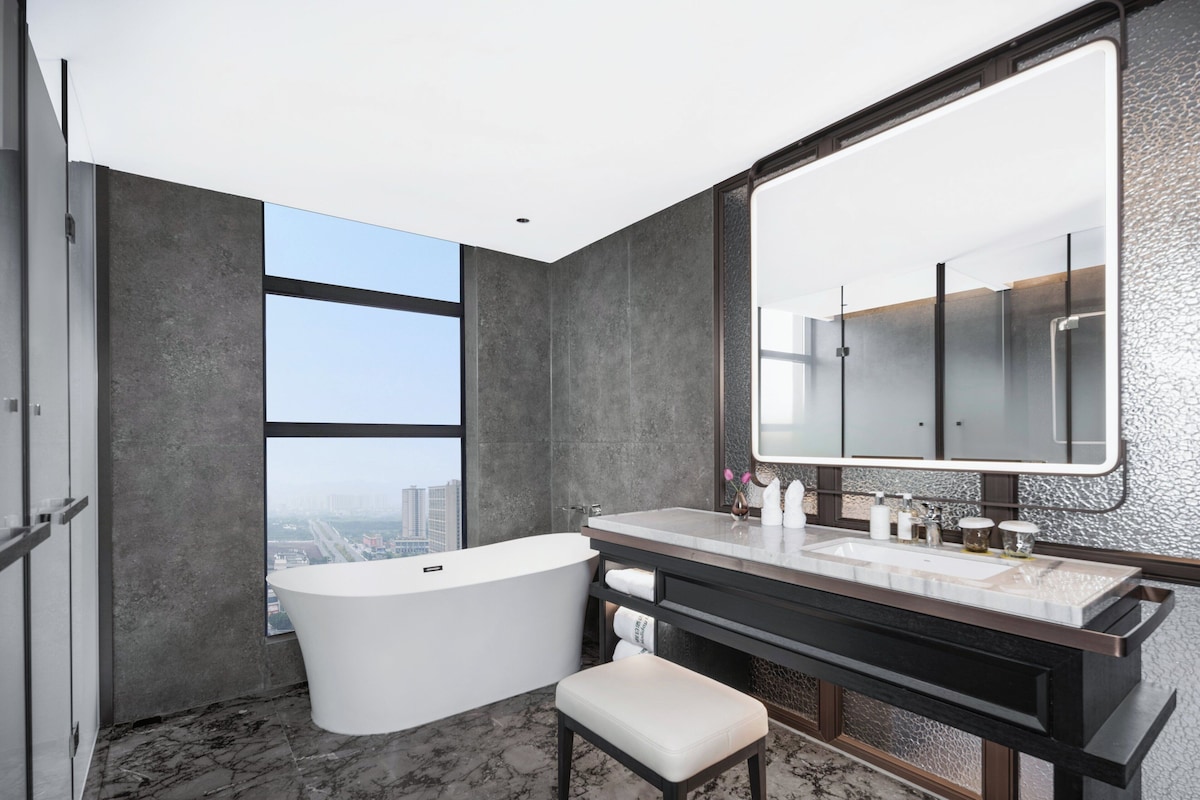 A modern bathroom with a freestanding bathtub, a large mirror, and a vanity with a marble countertop.