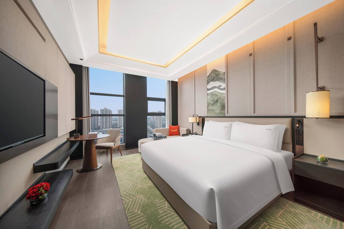 A modern hotel room with a large bed, a desk, a chair, and a TV.