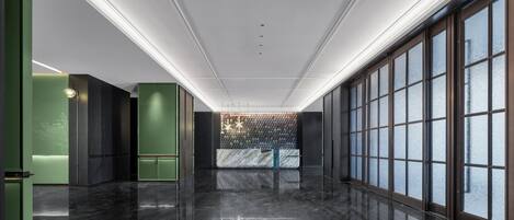 A modern hotel lobby with a polished marble floor, green accent walls, and large windows with frosted glass.