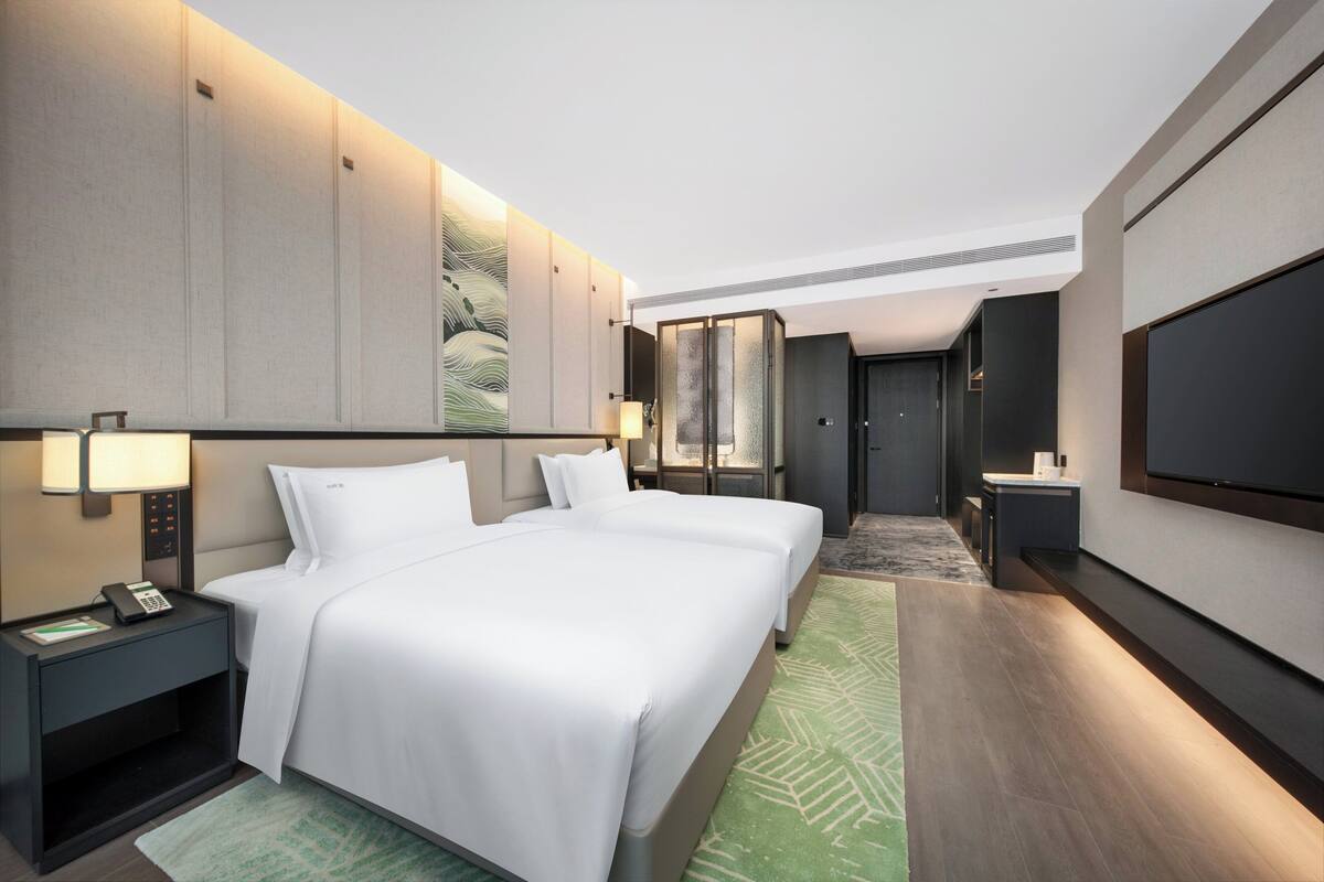 A modern hotel room with a large bed, bedside tables, a flat-screen TV, and a walk-in closet.