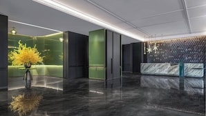 Eine moderne Lobby mit einem Marmor-Empfangstresen, grünen Akzentwänden und einer großen gelben Blumenkomposition.