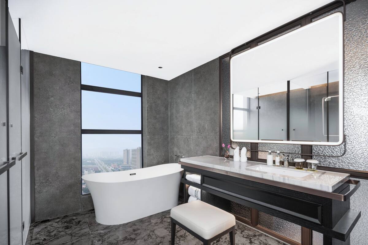 A modern bathroom with a freestanding bathtub, a large mirror, and a vanity with a marble countertop.