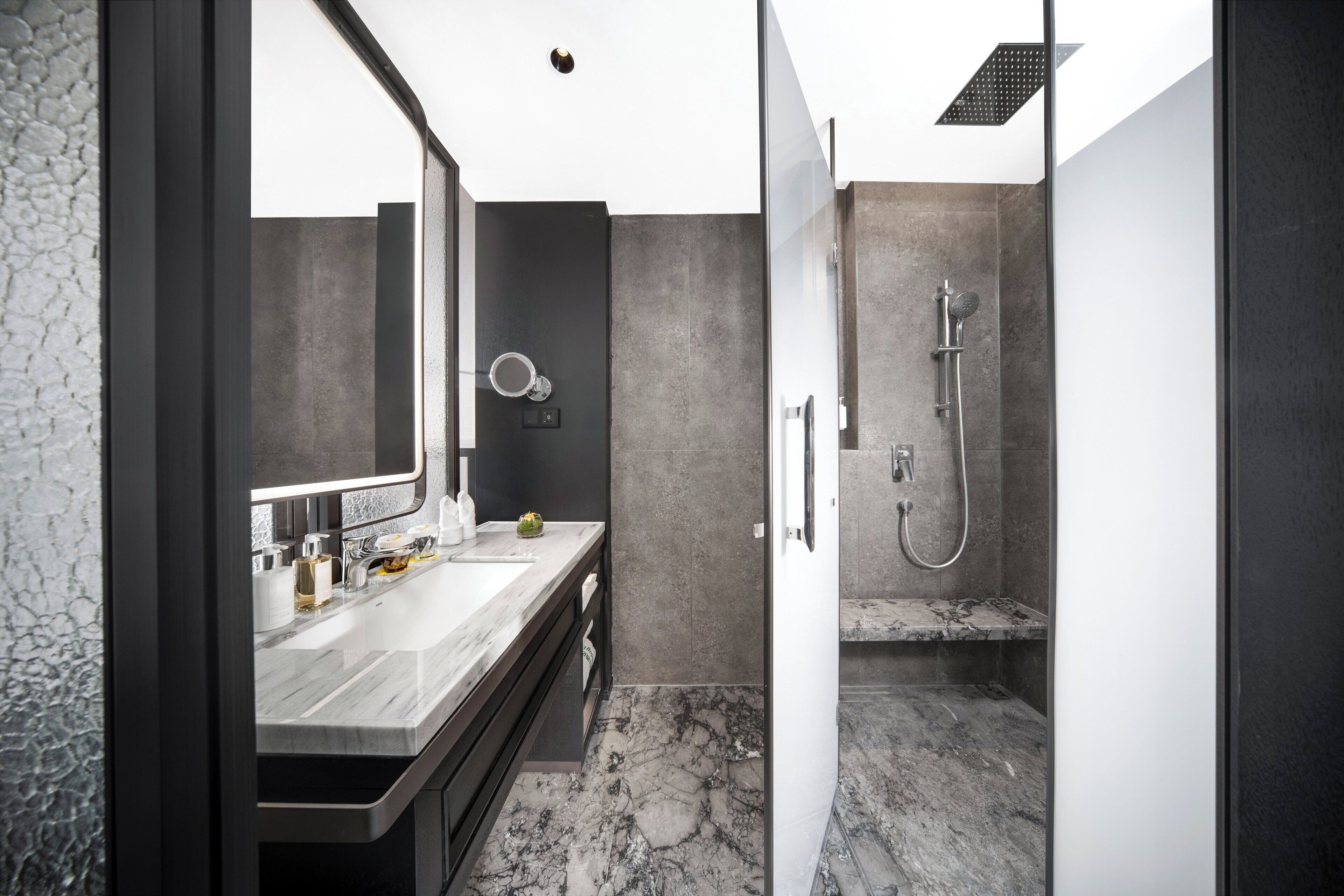 A modern bathroom with a marble sink, a large mirror, a shower with a handheld showerhead, and a textured wall.