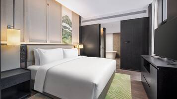 A modern hotel room with a large bed, bedside tables, a flat-screen TV, and a painting on the wall.