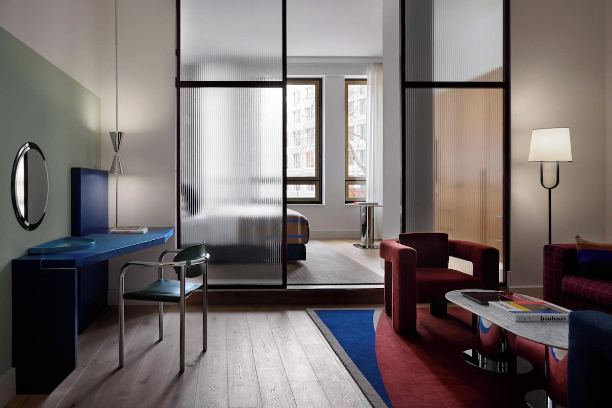 Ein modernes Hotelzimmer mit Schreibtisch, Stuhl, Sofa und Blick durch ein großes Fenster.