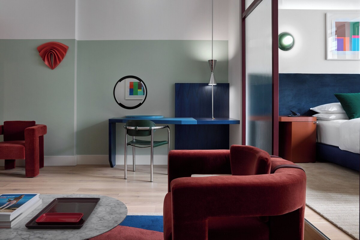 Ein modernes Hotelzimmer mit einem Bett, einem Schreibtisch, einem Stuhl und einem roten Schlafsofa.
