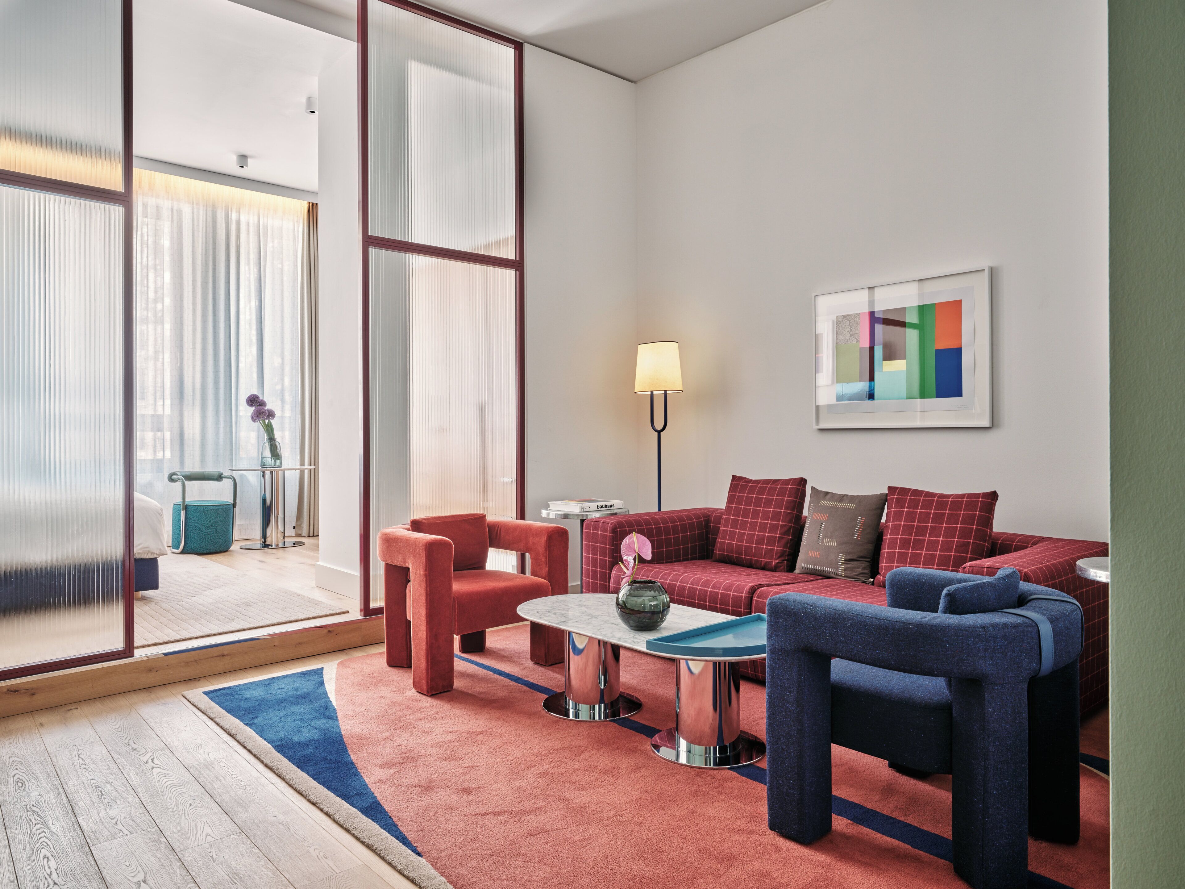 Un salon moderne avec un canapé rouge, des fauteuils bleus et une petite table basse.