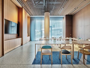 Une salle de conférence moderne, dotée d’une grande table, de chaises et d’un téléviseur fixé au mur.