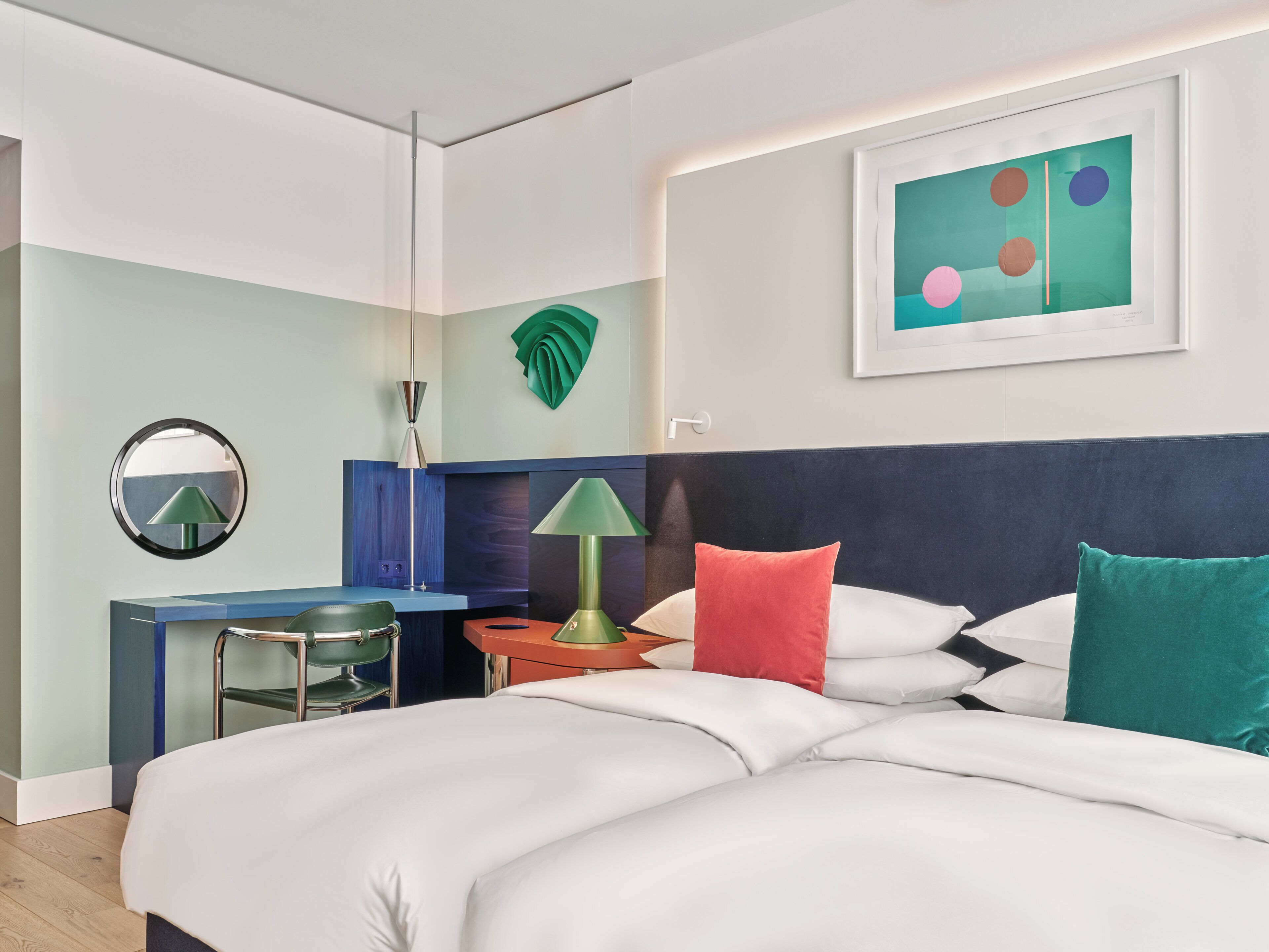 Habitació d'hotel amb un llit, un escriptori, una cadira, una làmpada i una obra d'art a la paret.