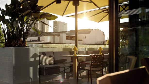 Een terras met een bank, stoelen en een tafel onder een gele parasol.