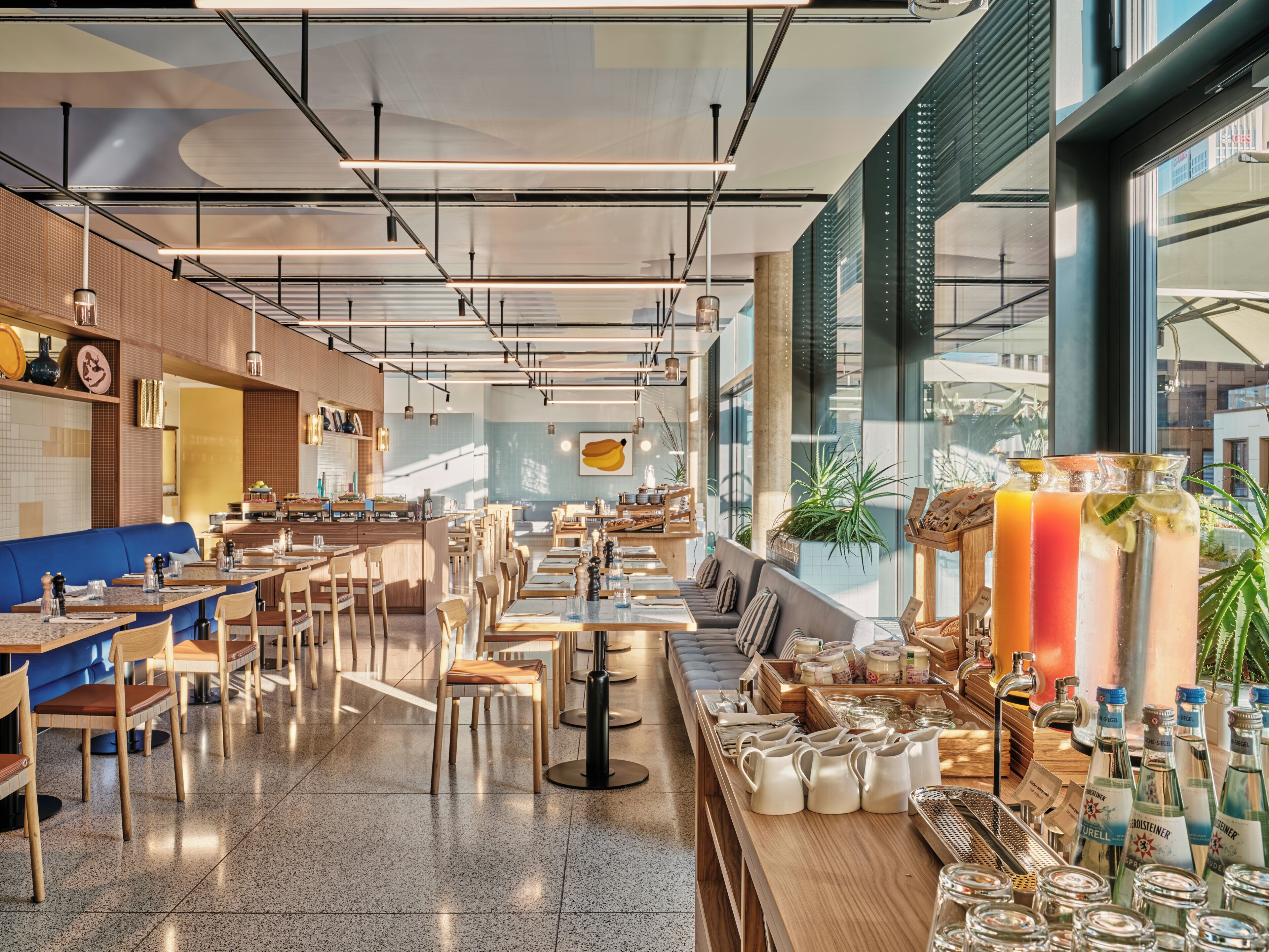 Interior de restaurant modern amb sostres alts, bigues fetes a la vista i diferents opcions d'asseients, incloent taules i seients privats.