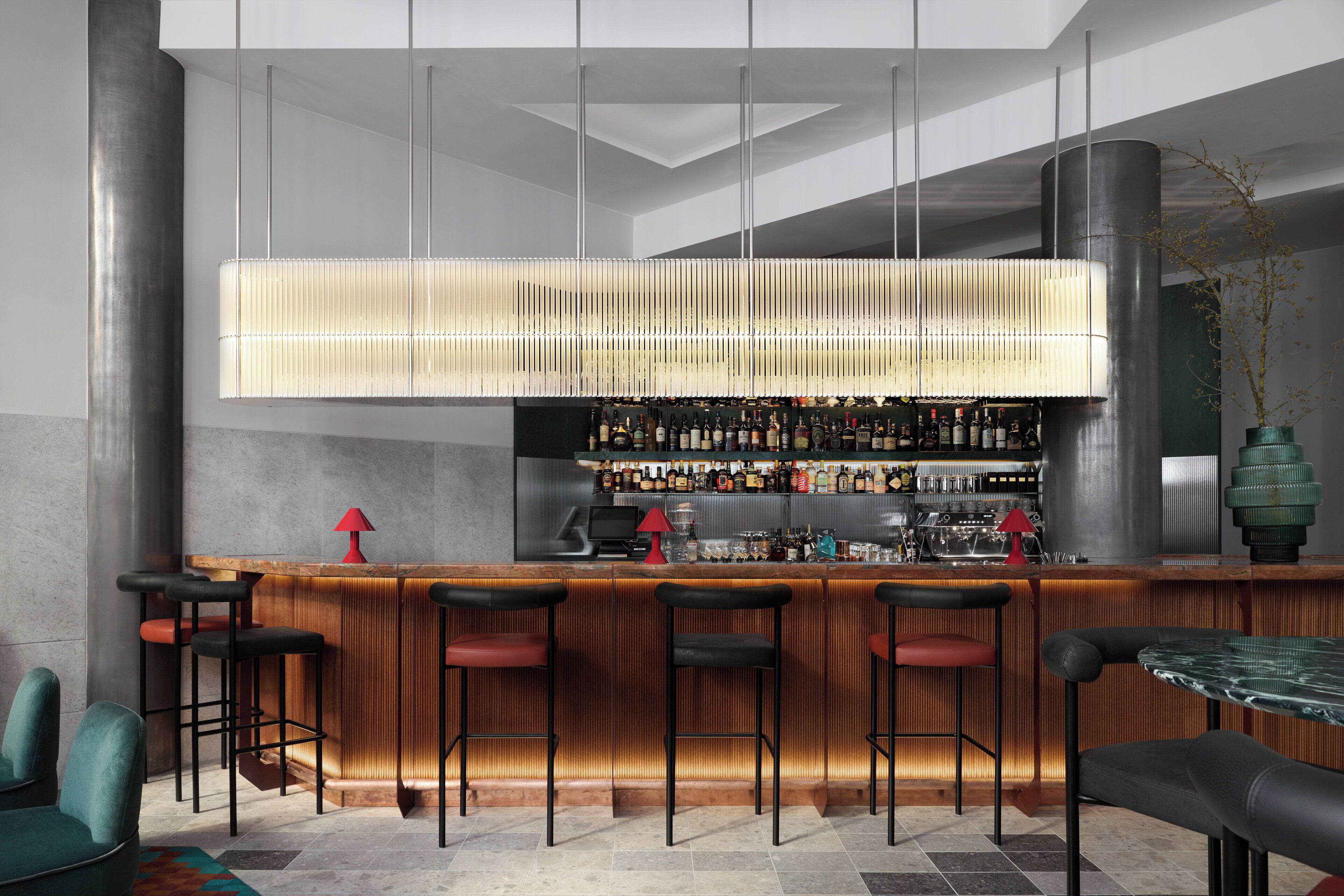 A modern bar area with a wooden counter, multiple stools, and a variety of bottles and glasses.