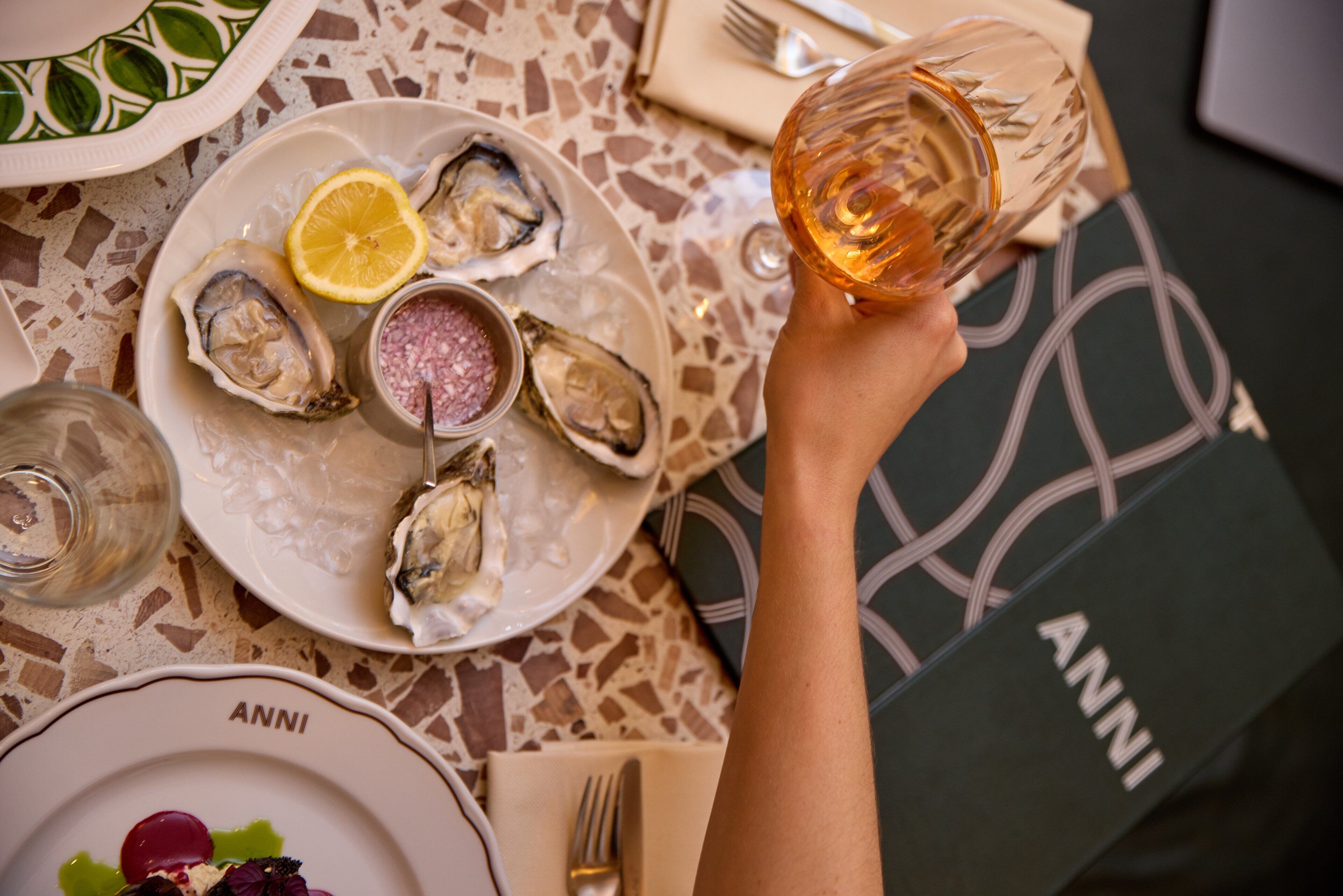 Una mesa de comedor con platos de ostras, una copa de vino y una servilleta.