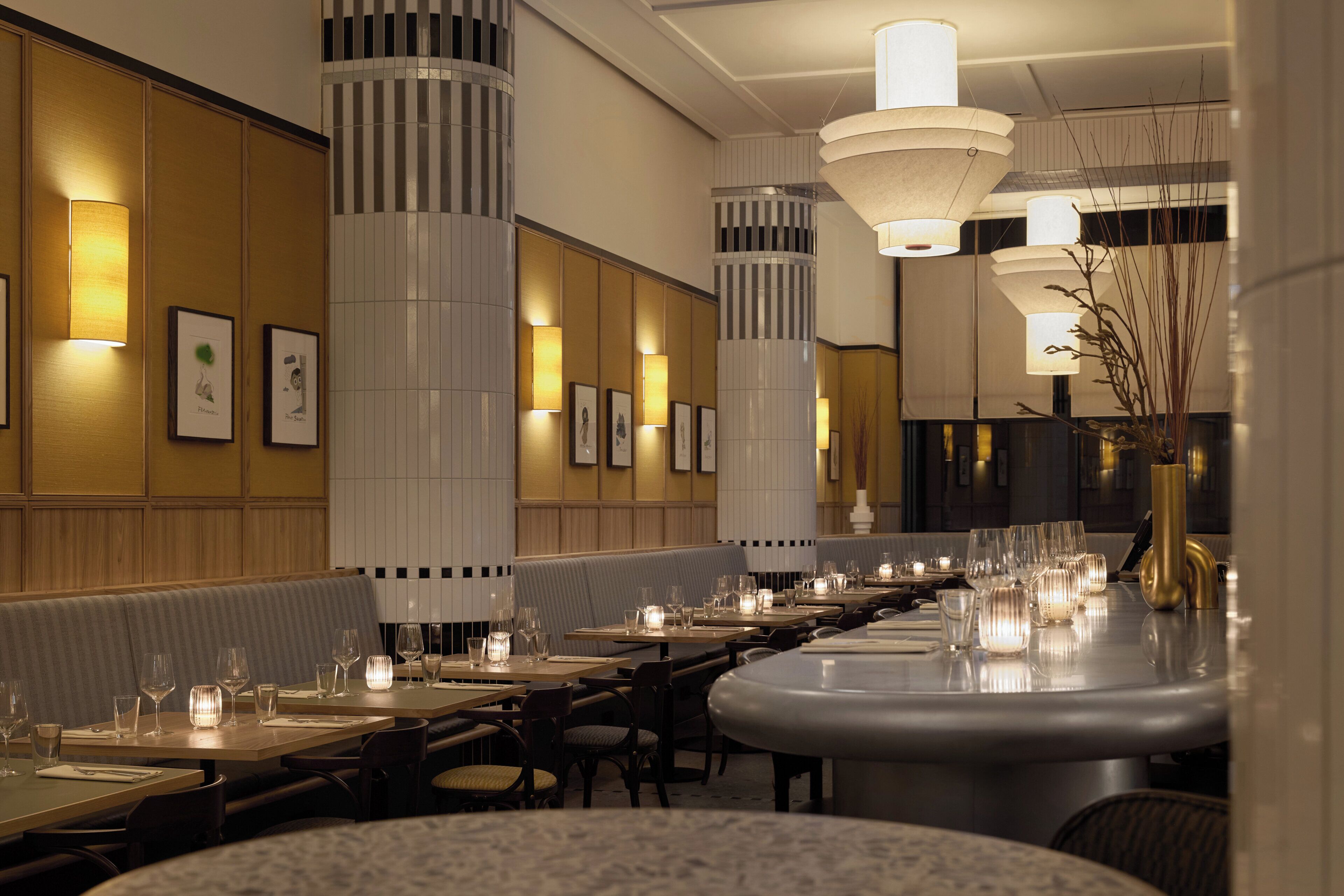 A restaurant with long tables, cushioned booths, and modern lighting fixtures.