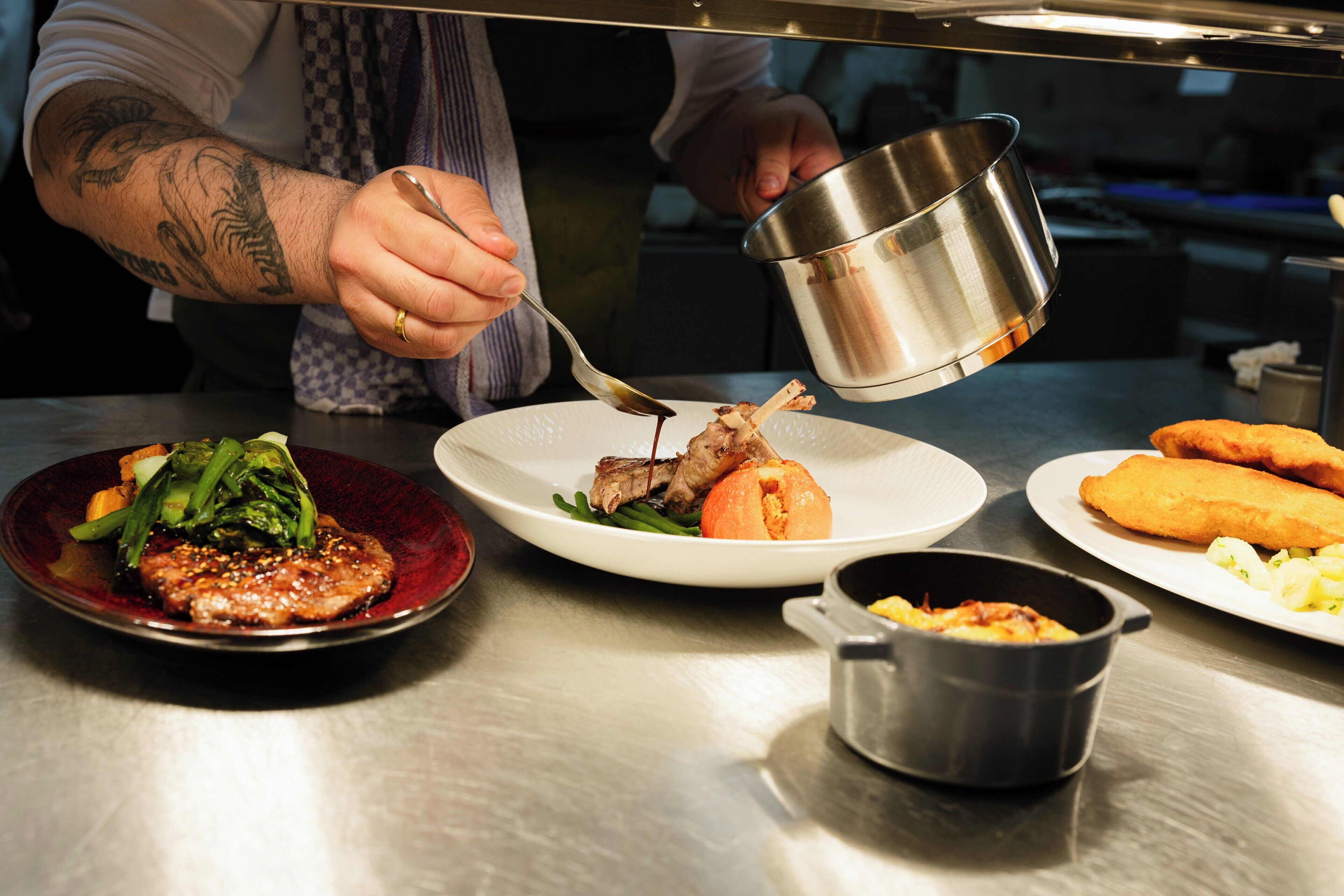 A chef pouring sauce onto a plate of food.