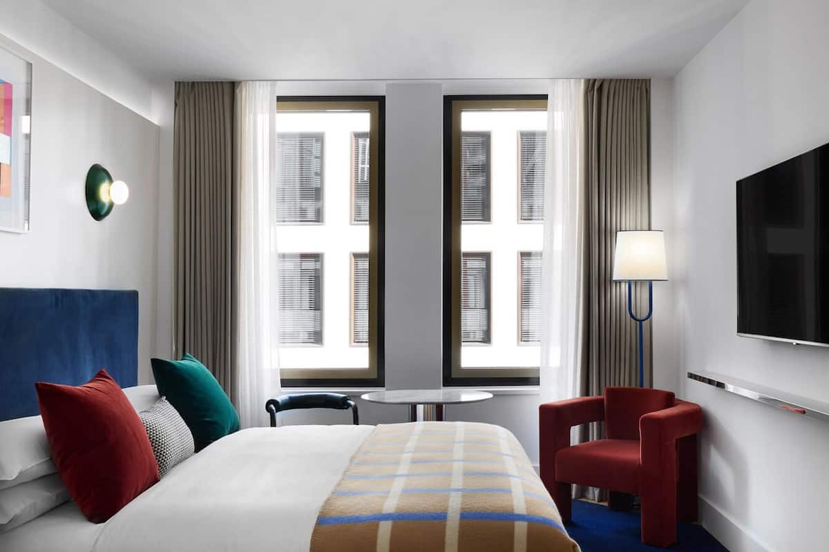 Ein Hotelzimmer mit einem großen Bett, einem Schreibtisch, einem Stuhl, einem Fernseher und einem Fenster mit Vorhängen.
