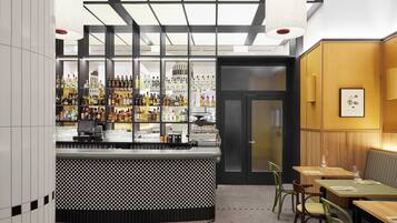 A bar area with a checkered counter, shelves of bottles, and a seating area with wooden tables and chairs.