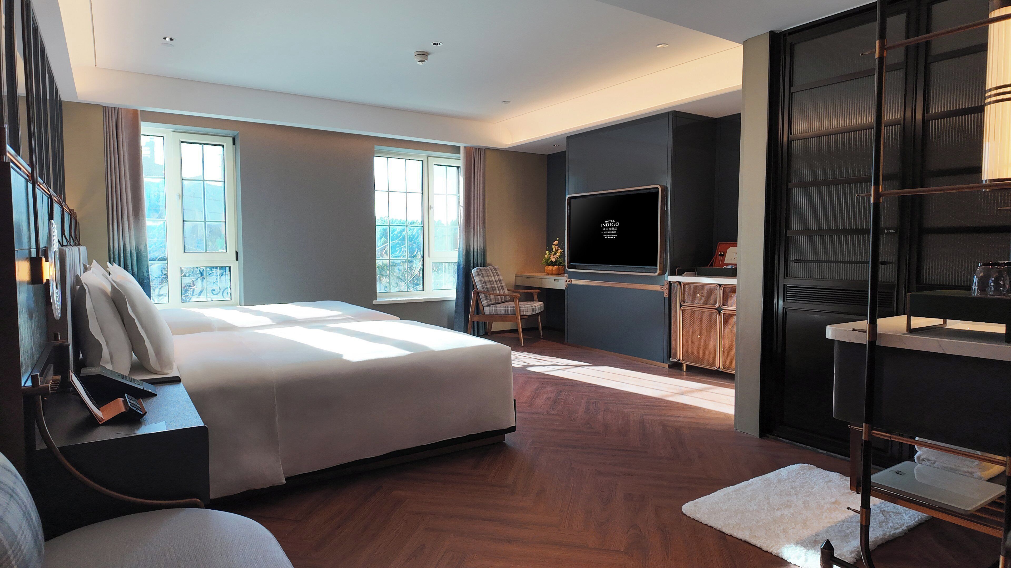 A modern hotel room with a large bed, a desk with a computer, a TV, and a seating area with a chair and a small table.