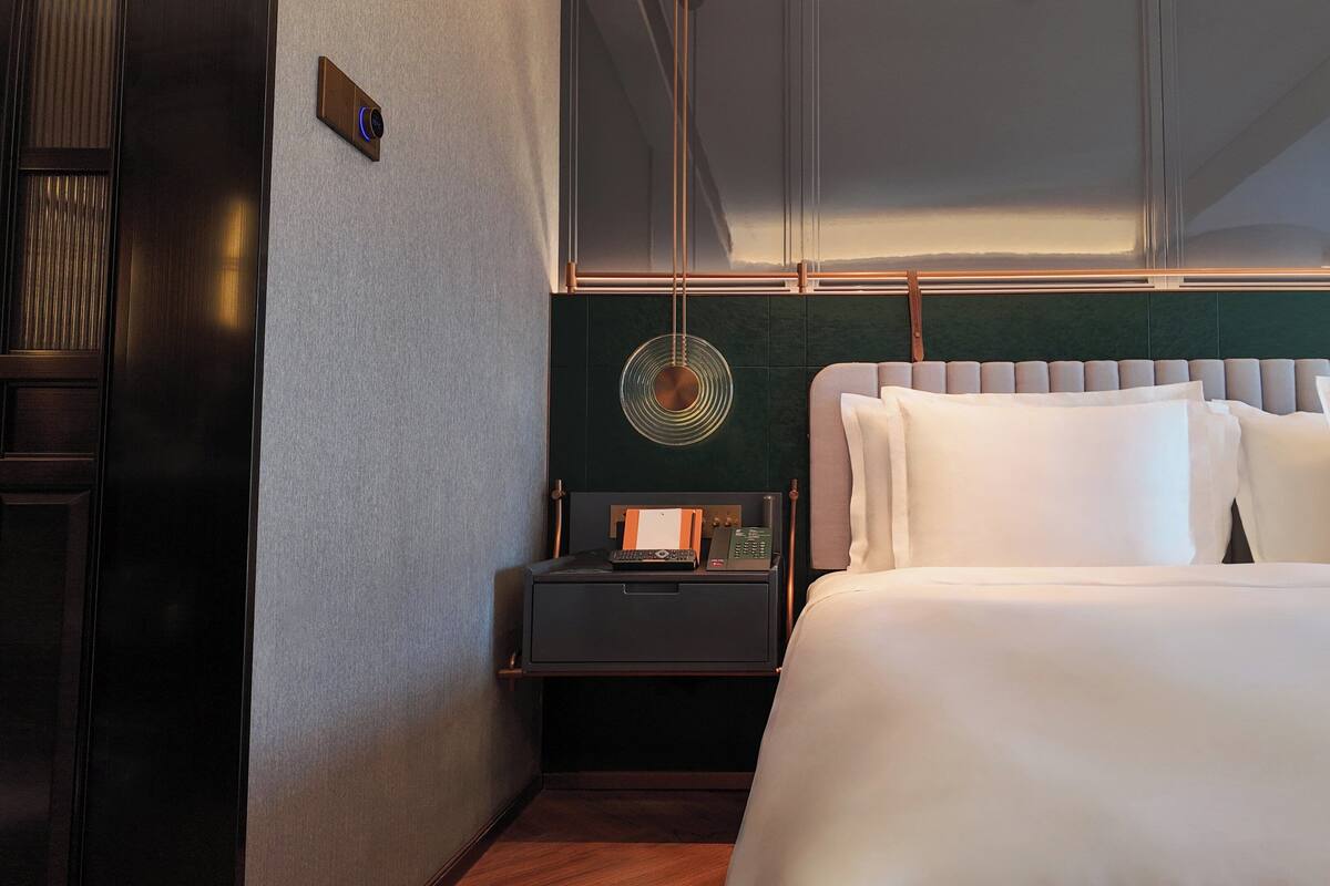 A modern hotel room with a large bed, a bedside table with a lamp, and a view of the mountains through the window.