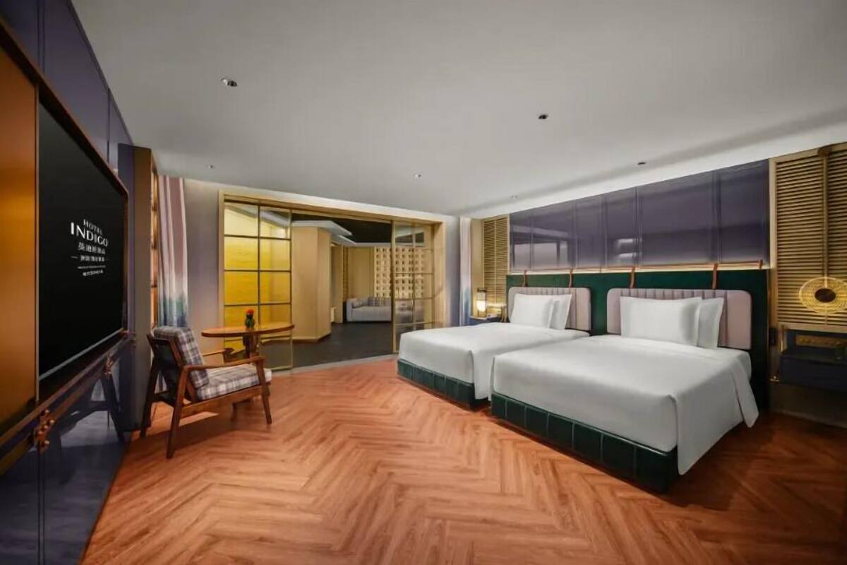 A hotel room with two beds, a TV, a wooden floor, and a view of the outside.