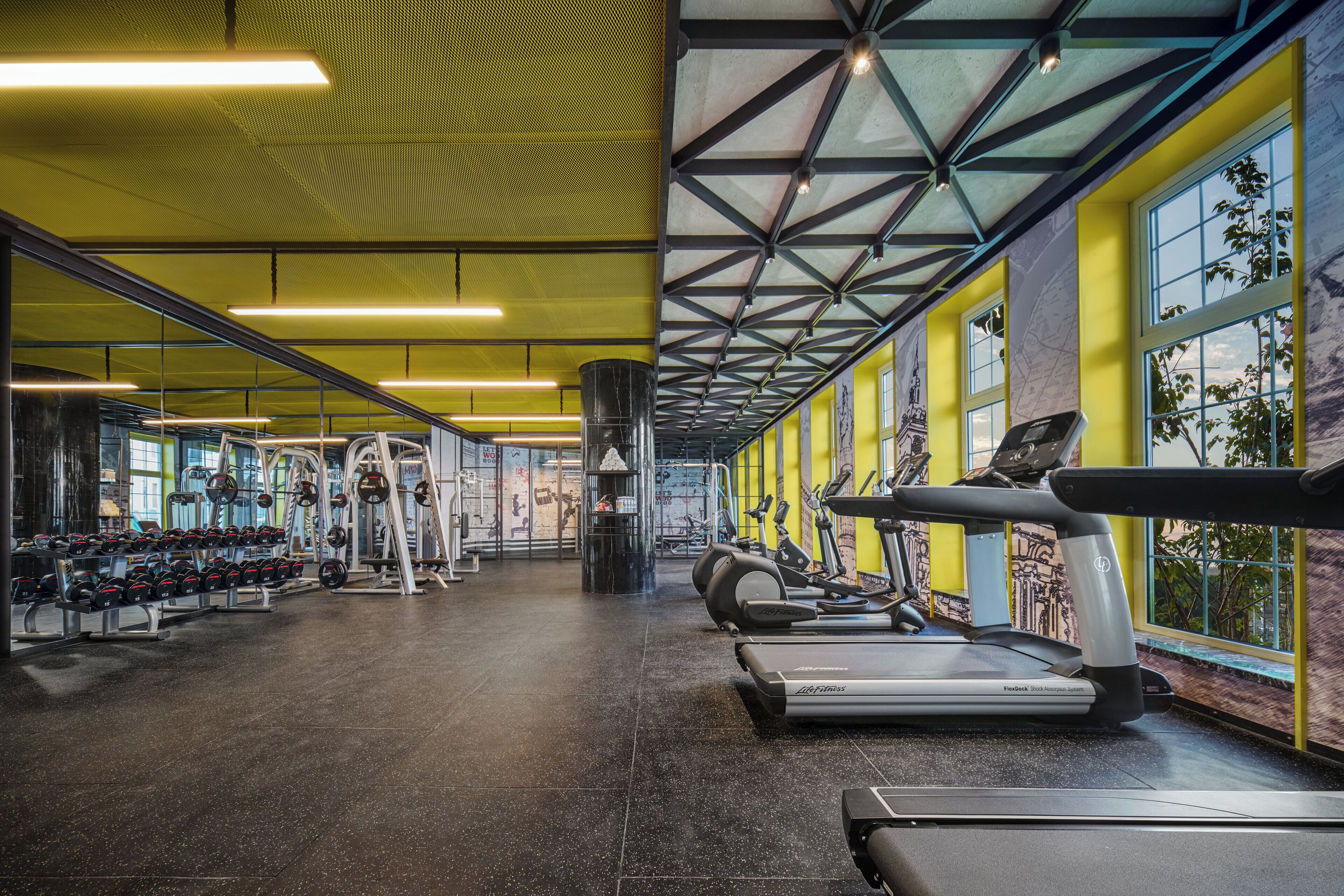 Une salle de sport équipée de matériel d’exercice, dotée d’un mur miroir et arborant une décoration aux couleurs jaune et bleu.
